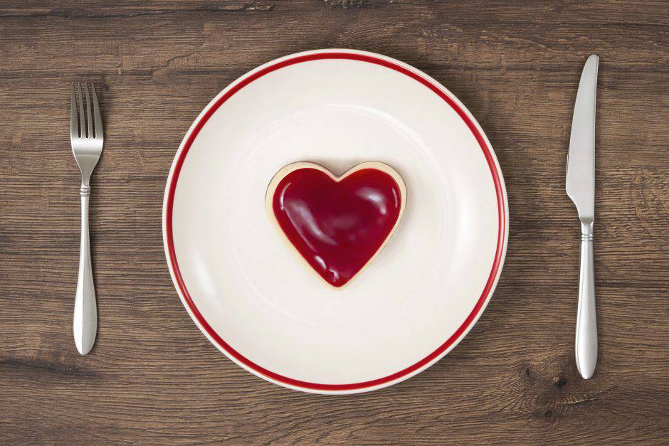 Heart shaped whole mini raspberry cheesecake on red stripe plate with fork and table knife on wooden rustic background.