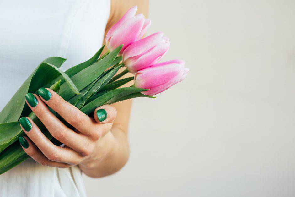 Female hands with green manicure holding pink tulips on a beige background. Copy space.
