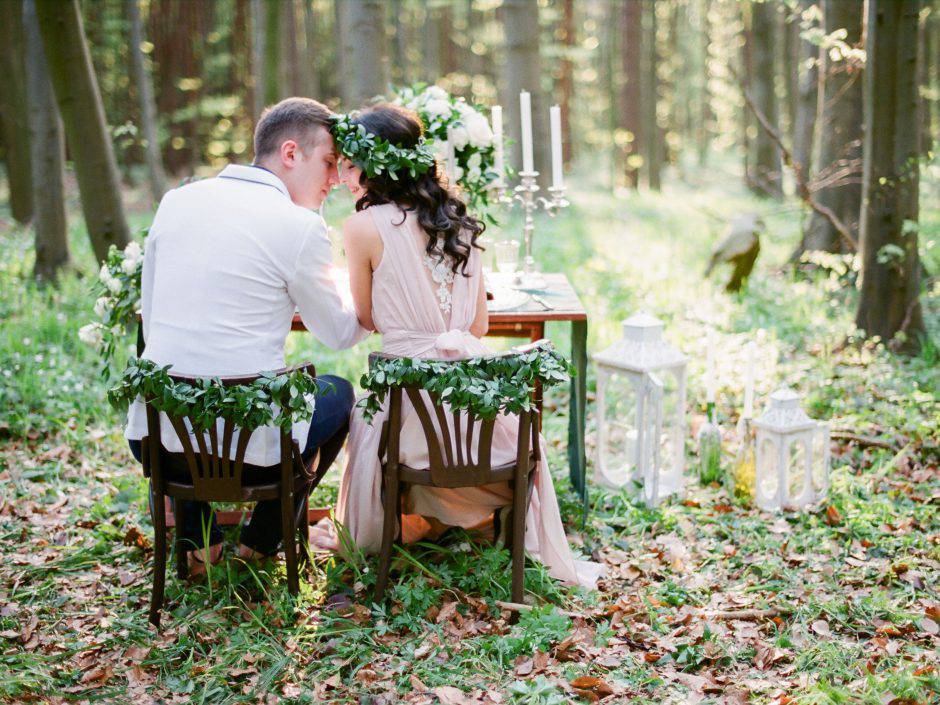 Groom and bride sitting at the table setted for two in the forest. Rustic style wedding in the woods.