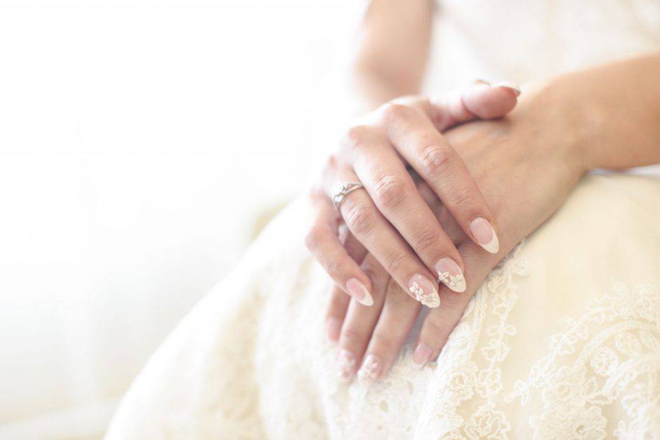 Bride's hand on her wedding dress with beautiful manicure. Unrecognizable caucasian female, close-up shot.