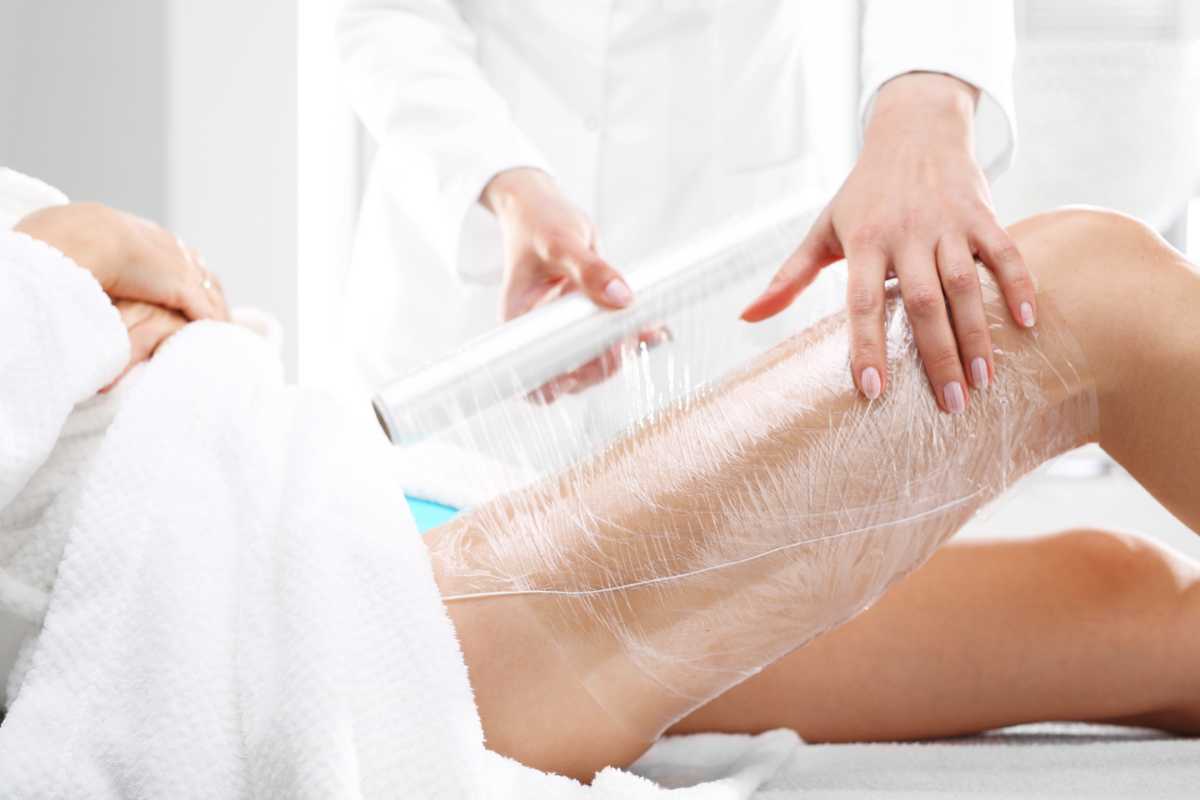 una ragazza avvolge la coscia in pellicola dopo aver applicato una crema anticellulite