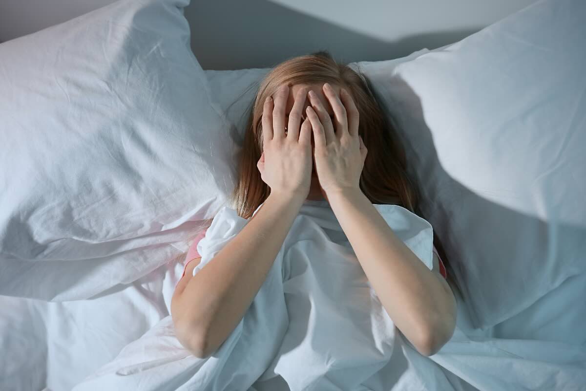 donna nel letto con mani sul volto 