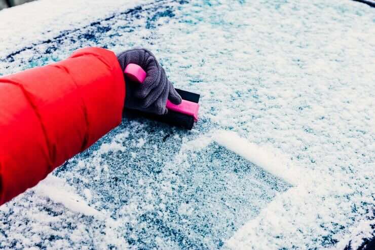 uomo toglie ghiaccio dal parabrezza
