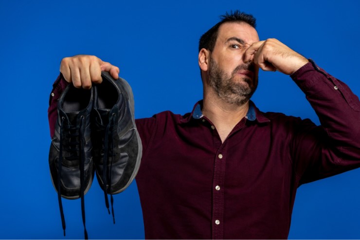 uomo che si tappa il naso con le scarpe in mano