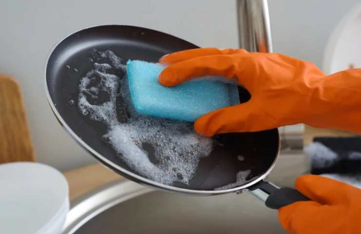 donna che pulisce padella con spugna