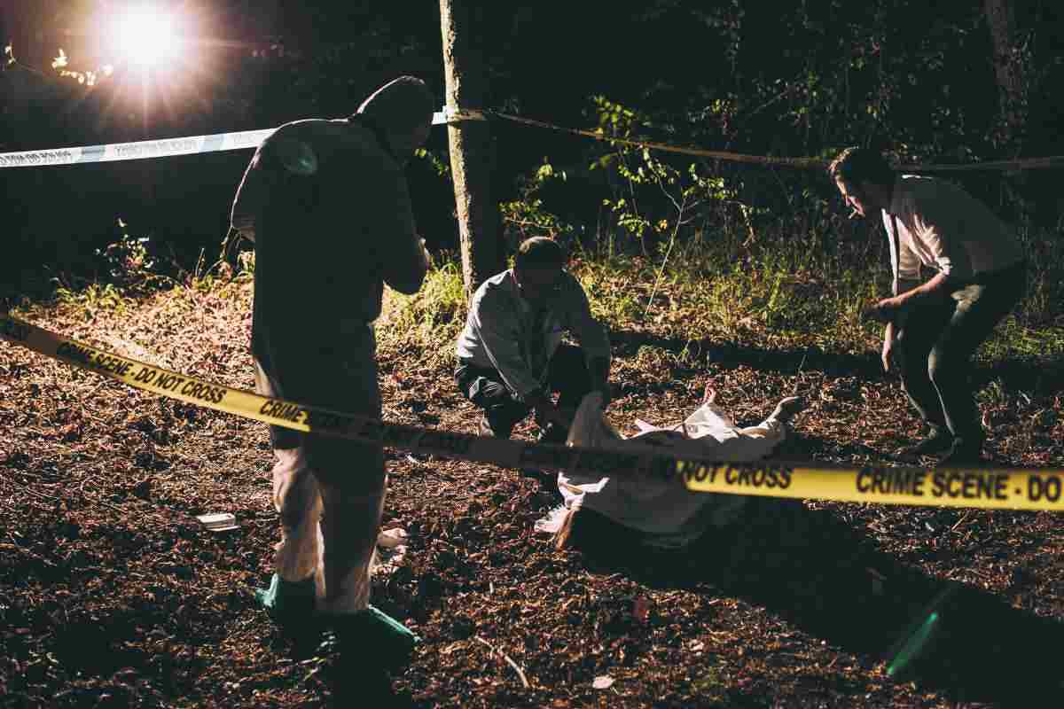La scena di un crimine con un corpo a terra circondato dal cordone giallo e degli uomini che indagano