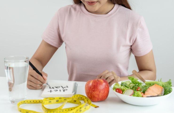 donna seduta a tavola con mela, bicchiere di acqua e metro