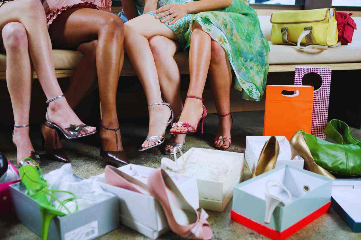 Tre donne sedute di cui si vedono solo le gambe che stanno provando diverse scarpe e delle scatole da scarpa in primo piano