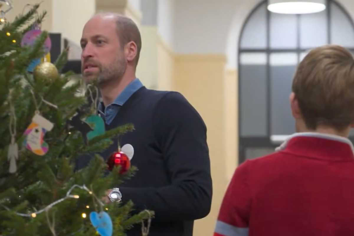 Il principe William addobba un albero di Natale, di spalle il principe George sulla destra con un maglione rosso