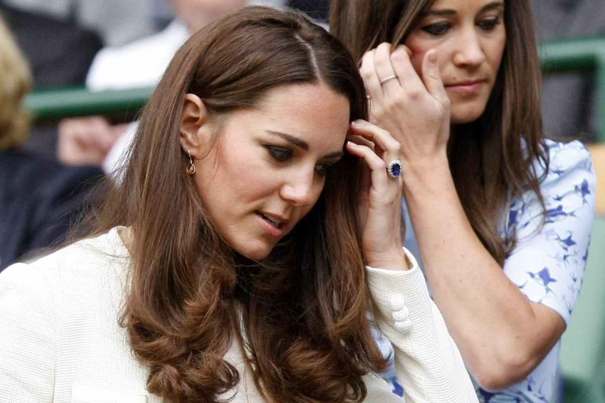 Kate Middleton con il volto chinato si sistema i capelli 