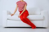 Una ragazza con indosso una maglietta a righe bianco rosse, una gonna rossa e i collant rossi seduta su un divano bianco