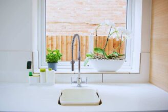 Il bancone di una cucina con il lavabo, alle spalle una finestra e alcune piante: un'orchidea e del basilico