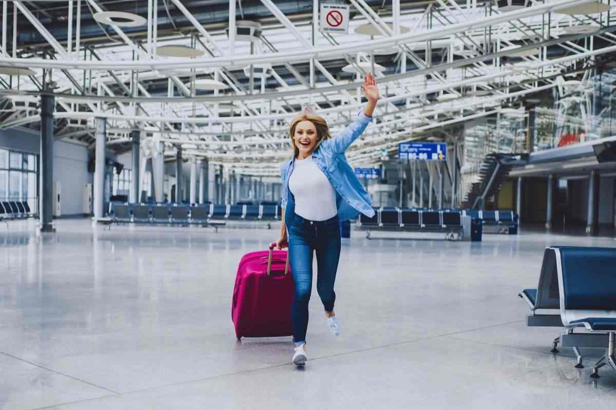 Una ragazza corre in aeroporto con un trolley nella mano destra agitando la sinistra