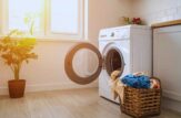 Una lavatrice con lo sportello aperto accanto dei panni da lavare, sullo sfondo una pianta e una finestra