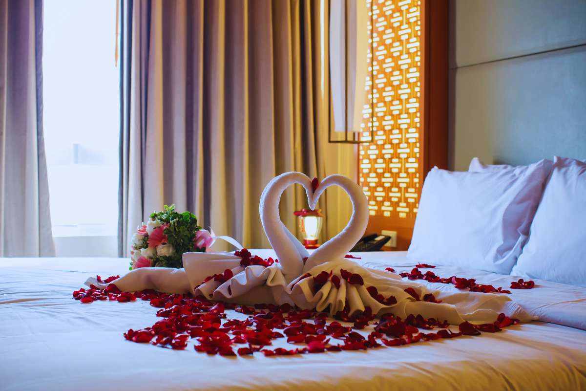 Due cigni di stoffa su un letto con dei petali di rosa